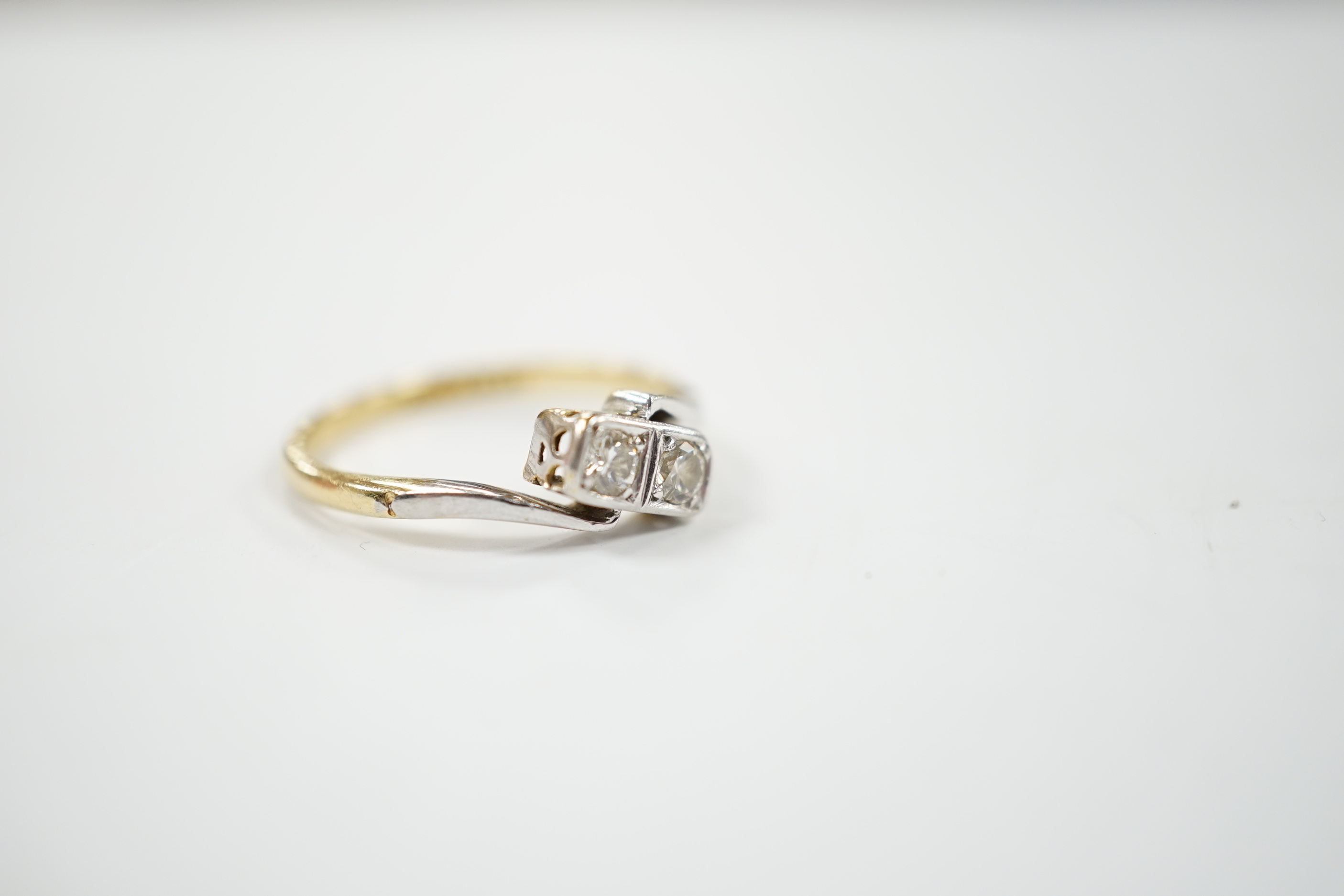 An 18ct, plat and two stone diamond set crossover ring, size M, gross weight 2.3 grams.